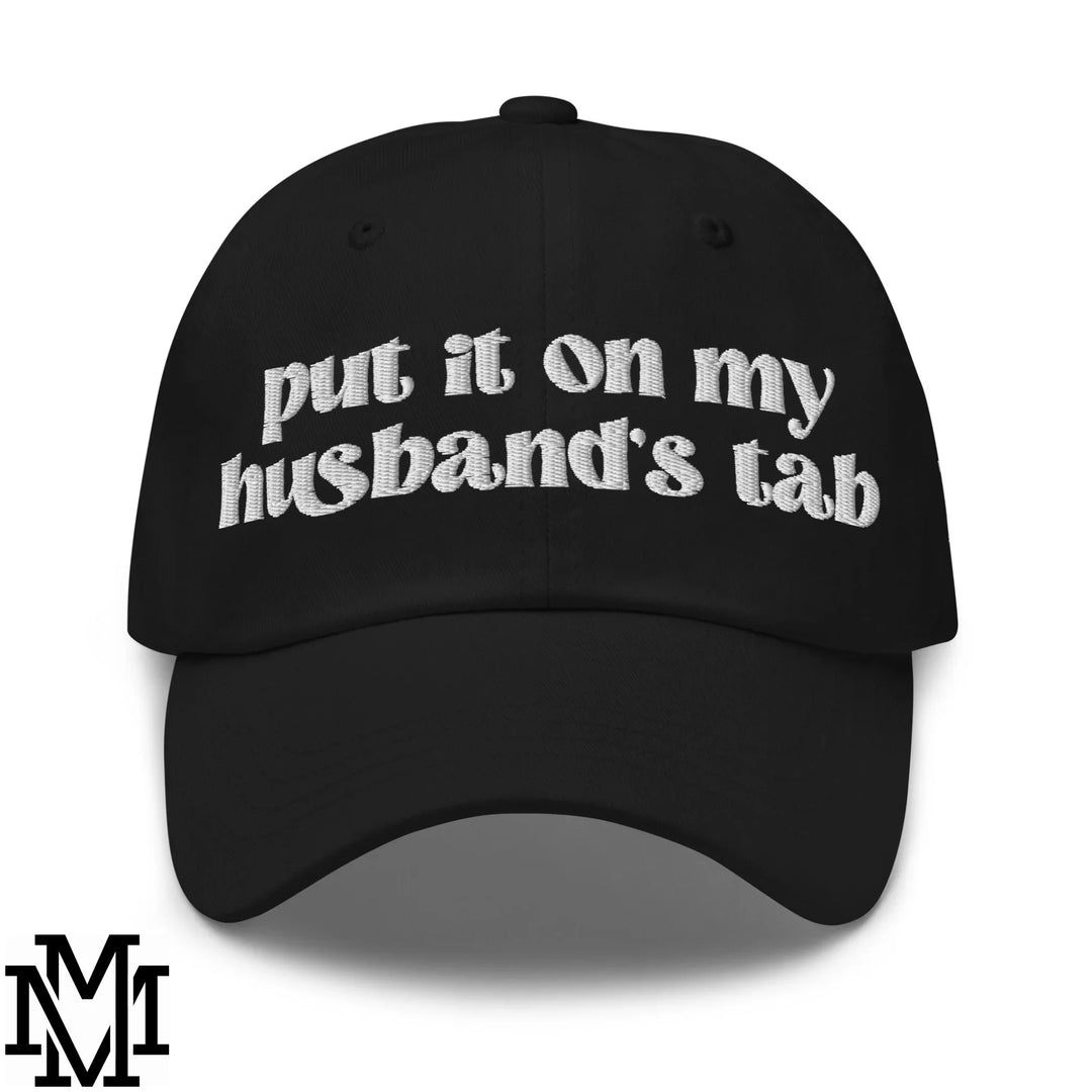 Black baseball cap with white embroidered put it on my husbands tab text showcasing effortless humor dad hat style