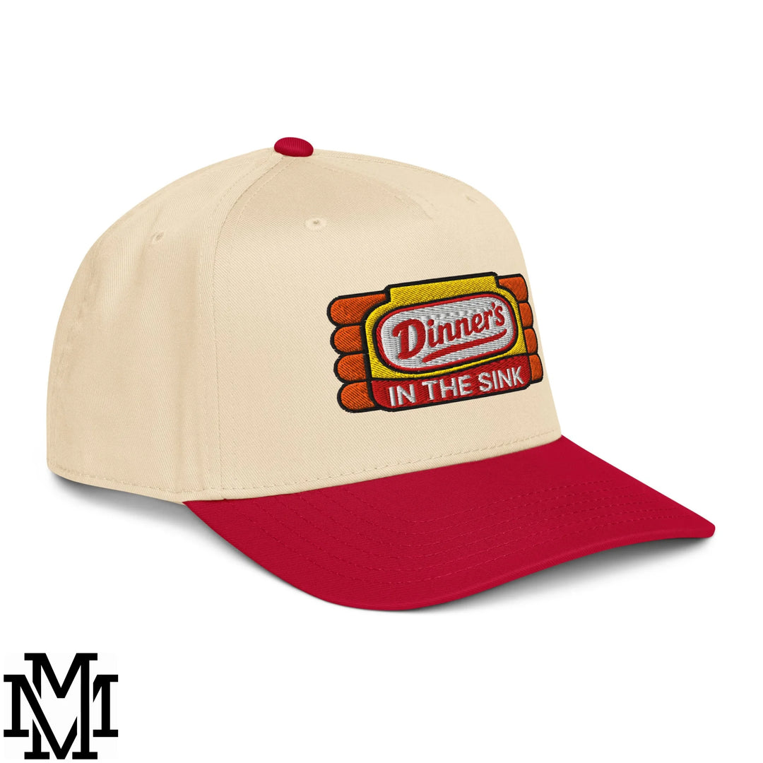 Cream-colored baseball snapback hat with red brim and dinner’s in the sink embroidered logo on yellow background