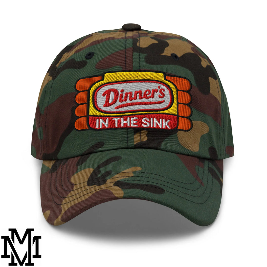 Camouflage unstructured dad hat with embroidered dinners in the sink logo patch in green and beige colors