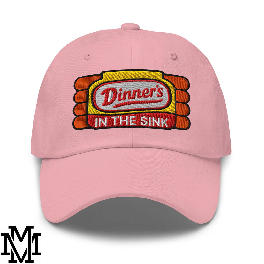 Pink unstructured dad hat with embroidered diner-style sign logo dinner’s in the sink in red white and yellow stitching