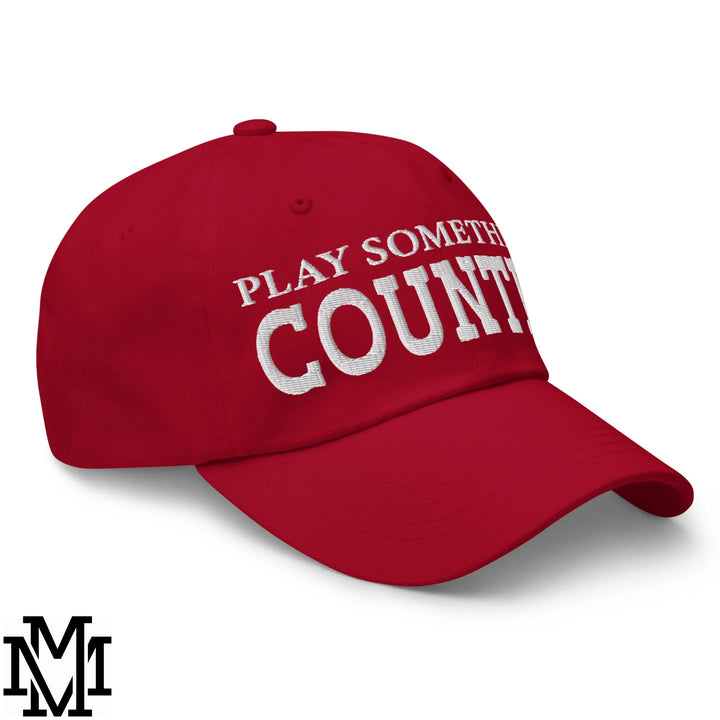 Red unstructured dad hat made of cotton with white embroidered text play something country on the front